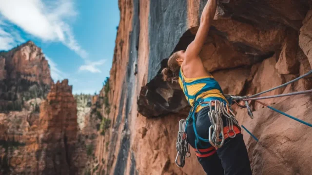 climber scaling a rock face with a brightly colored climbing harness, showcasing essential safety gear for rock climbing.