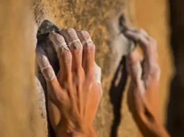 Climber's hands, one with fingers expertly taped for maximum support, gripping a rock hold, visually explaining how to tape fingers for climbing health and strength.