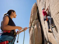 Climbing: How to Belay? Your Ultimate Answer Female belayer expertly managing rope for a male climber on a sunlit rock face, illustrating the ultimate answer to how to belay in climbing.