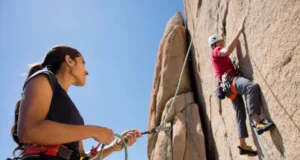 Climbing: How to Belay? Your Ultimate Answer Female belayer expertly managing rope for a male climber on a sunlit rock face, illustrating the ultimate answer to how to belay in climbing.