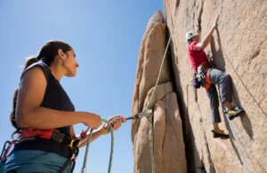 Climbing: How to Belay? Your Ultimate Answer Female belayer expertly managing rope for a male climber on a sunlit rock face, illustrating the ultimate answer to how to belay in climbing.