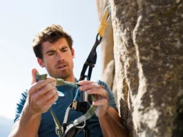 Male climber inspecting his rock climbing harness for peak safety, demonstrating harness know-how, relevant for climbers learning how to tape fingers for climbing.