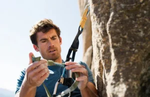 Unlock Peak Safety: Rock Climbing Harness Know-How Male climber inspecting his rock climbing harness for peak safety, demonstrating harness know-how, relevant for climbers learning how to tape fingers for climbing.