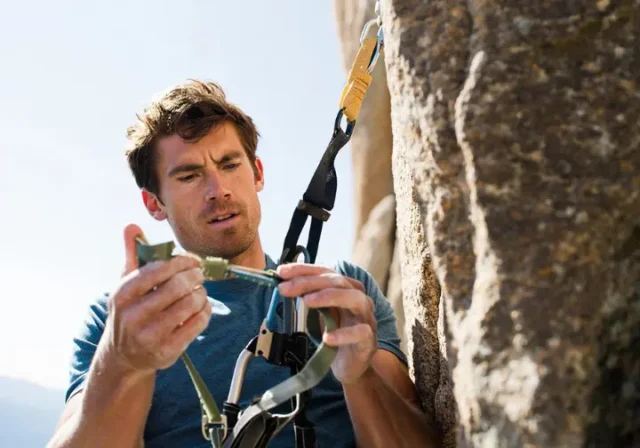 Male climber inspecting his rock climbing harness for peak safety, demonstrating harness know-how, relevant for climbers learning how to tape fingers for climbing.