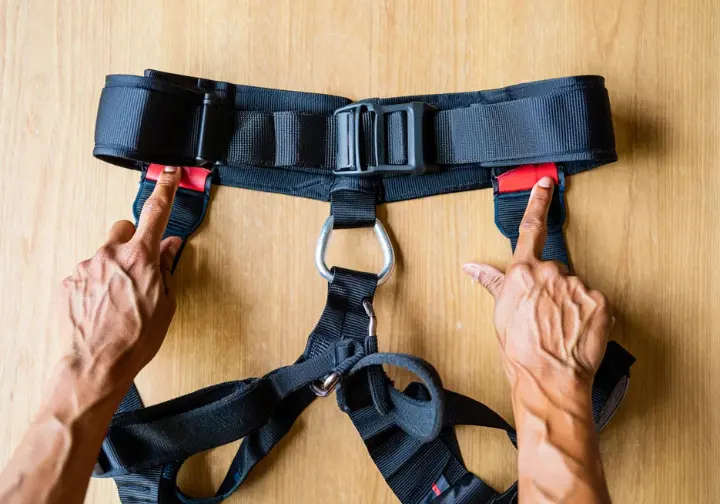 Detailed view of climbing harness anatomy and essential components, with diverse hands pointing them out, useful for climbers also learning how to tape fingers for climbing.