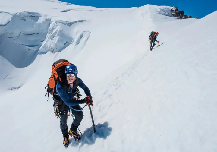 Understanding Rainier's physical demands: Climber ascending steep snow slope with a heavy backpack.