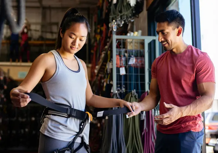 Climber getting assistance with selecting and sizing a climbing harness for a perfect fit, important for overall climbing safety including knowing how to tape fingers for climbing.