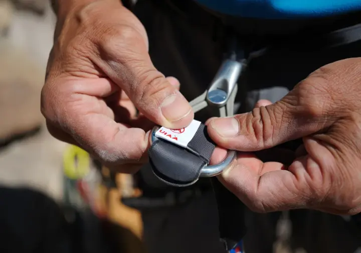 Close-up of hands inspecting a climbing harness for safety, highlighting standards and retirement criteria, crucial for climbers who also learn how to tape fingers for climbing.