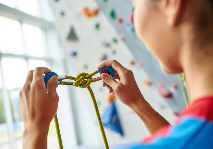 Climber's hands mastering harness usage by securely tying a figure-eight knot, a peak safety technique, relevant alongside learning how to tape fingers for climbing.