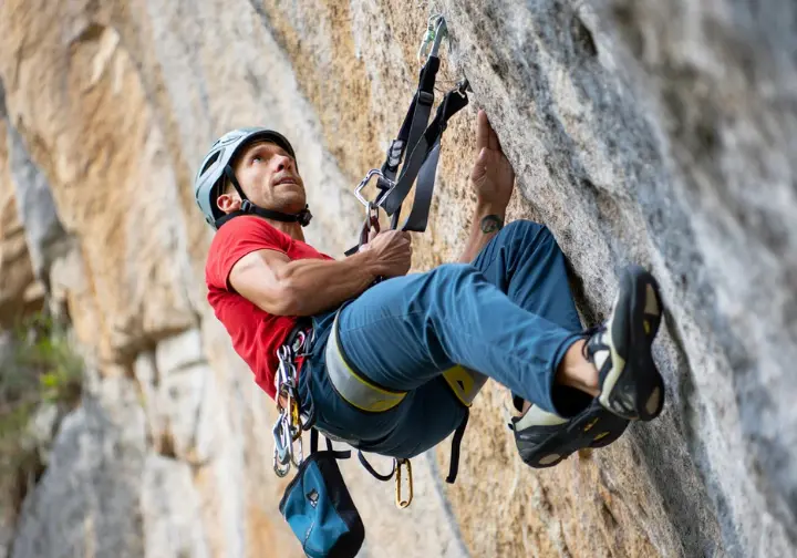 Climber demonstrating the use of suspension trauma relief straps for advanced safety, crucial knowledge for those learning how to tape fingers for climbing and overall climbing safety.