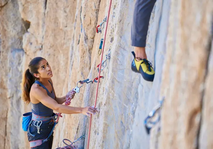 Experienced female belayer demonstrating advanced belay skills and rope management for a lead climber, as part of advancing how to belay techniques.