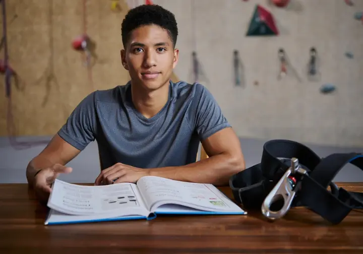 Climber intently studying a climbing safety manual, symbolizing the belayer's ethos of responsibility and continuous learning in how to belay.