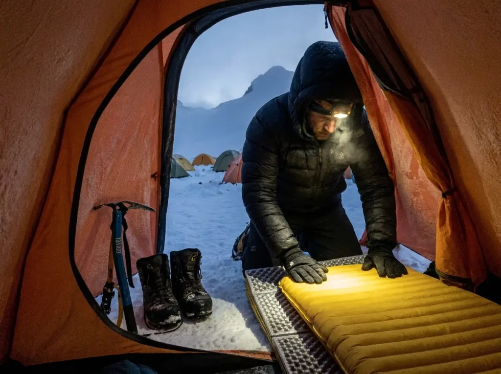 Climber doubling sleeping pads in a tent at Camp Muir before a midnight alpine start on Rainier
