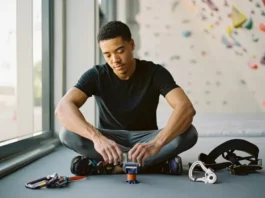 A climber confidently inspects their first set of belay equipment, including a harness and various belay devices, preparing for their climbing journey.
