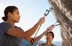 The Ultimate Quickdraw Guide: How to Choose & Clip Two rock climbers, male and female, demonstrating quickdraw use on a sunny rock face, highlighting how to choose and clip quickdraws for climbing safety.
