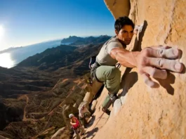 Two diverse climbers on a sunlit limestone cliff, showcasing various rock climbing styles available in Spain, with mountains and coastline in the background. Represents a definitive guide to rock climbing in Spain.