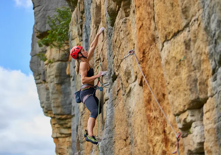 A detailed close-up of a climbing quickdraw, showing its components like carabiners and dogbone, fixed to a rock bolt, illustrating quickdraw foundation.