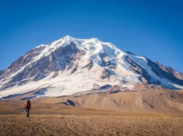 Panoramic view of a towering snow-covered peak in the Peruvian Andes, with a tiny mountaineer figure in the distance, illustrating an expert guide to mountaineering in Peru.