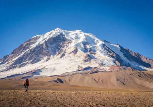 Panoramic view of a towering snow-covered peak in the Peruvian Andes, with a tiny mountaineer figure in the distance, illustrating an expert guide to mountaineering in Peru.
