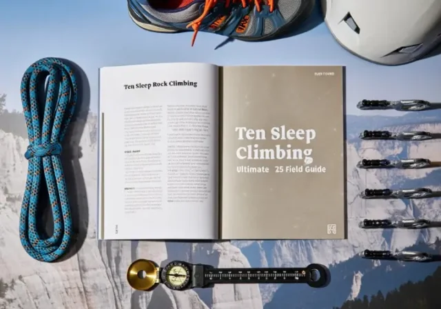 An open Ten Sleep rock climbing '25 field guide surrounded by climbing gear, with Ten Sleep Canyon in the background, symbolizing a comprehensive resource.