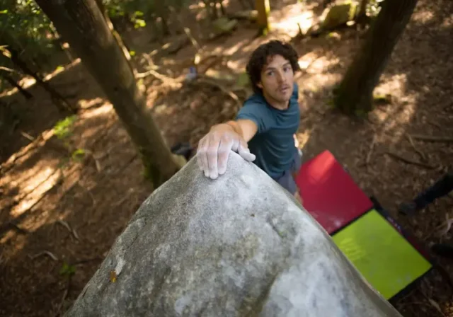 Climber at the summit of a distinctive granite boulder at Boat Rock bouldering area, symbolizing a deep dive into SCC conservation, unique granite features, and bouldering challenges.