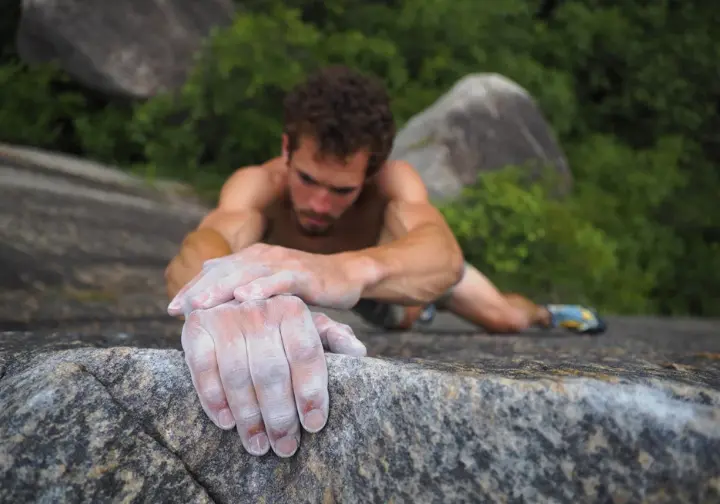 Close-up of a climber's hands and feet skillfully engaging with a unique granite slab formation at Boat Rock bouldering area, Atlanta's granite playground, highlighting the rock's texture.