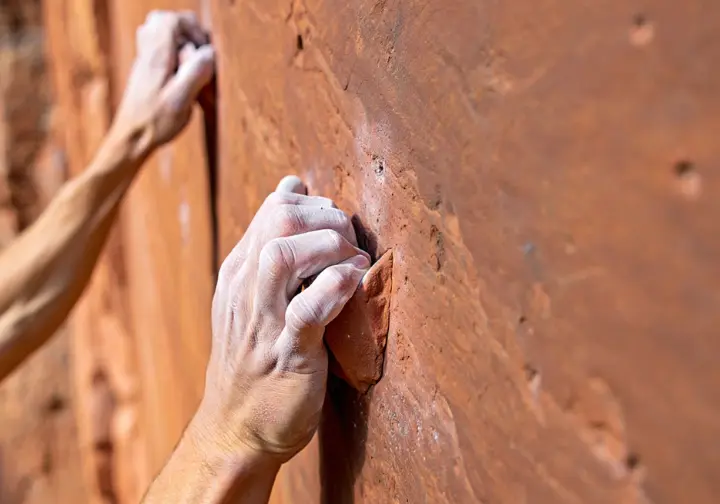 Close-up of a climber's hands on the unique pocketed Corbin sandstone of the Red River Gorge, representing its distinct geology and climbing style.