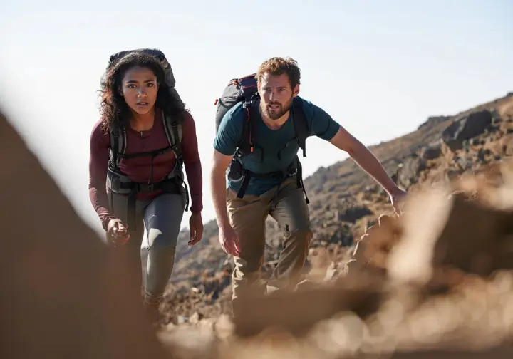 Two diverse climbers in active preparation, training on a steep trail with backpacks for their mountain climbing Kilimanjaro expedition.