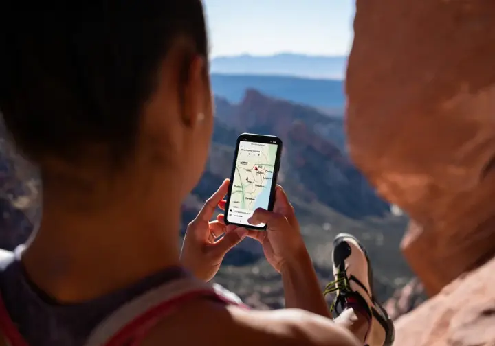 Climber using a smartphone map app to navigate key bouldering areas in Red Rock Canyon, with a scenic overlook of the diverse landscape.