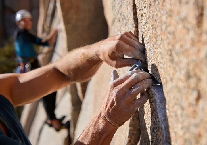 Close-up of a mountaineer's hands placing trad climbing gear on a Sierra Nevada rock face, demonstrating essential mountaineering skills.