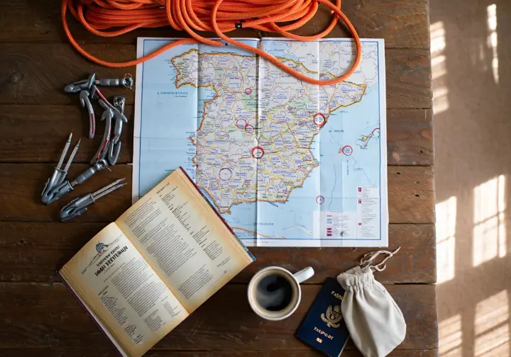 Flat-lay of climbing gear, map of Spain, and guidebook for planning an ultimate rock climbing adventure in Spain.