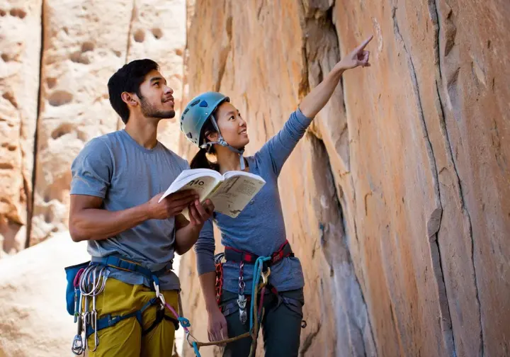 Two diverse climbers studying a guidebook at the base of a Ten Sleep Canyon crag, planning their rock climbing hit list.