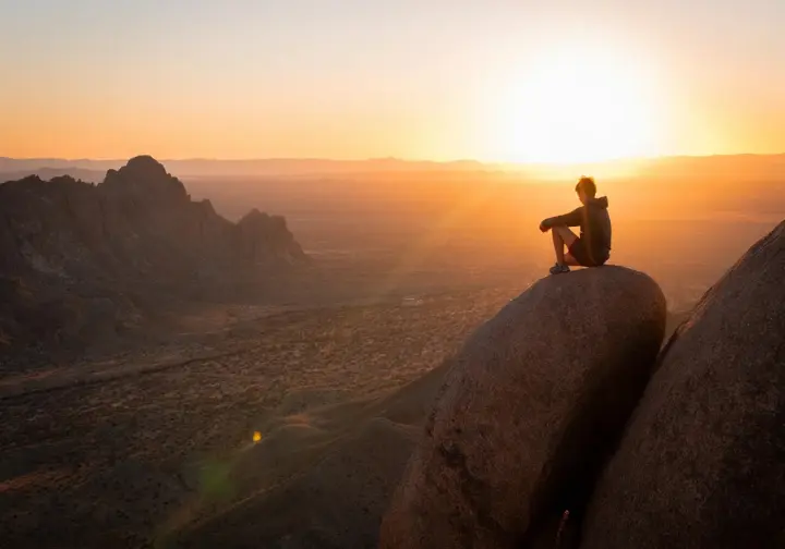 Silhouette of a climber on a boulder overlooking the Big Bend landscape at sunset, capturing the adventurous vibe of the Big Bend bouldering area.