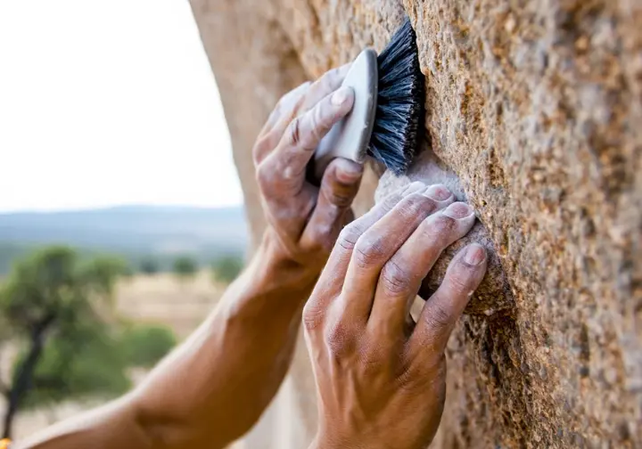 Climber's hands responsibly brushing chalk off a rock hold in Spain, highlighting safety, ethics, and environmental care in rock climbing.