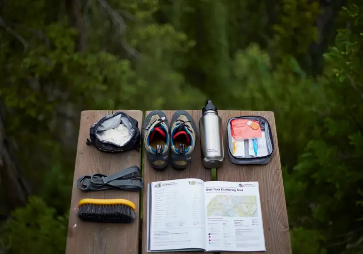 Essential bouldering gear for a Boat Rock adventure, including climbing shoes, chalk, guidebook, and water bottle, neatly arranged for planning a trip to the bouldering area.