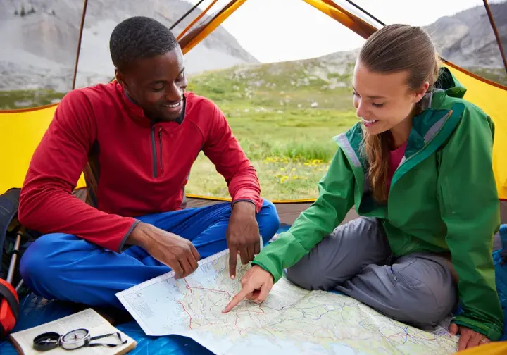 Two diverse mountaineers planning their expedition with a map and guidebook inside a tent in the Sierra Nevada.