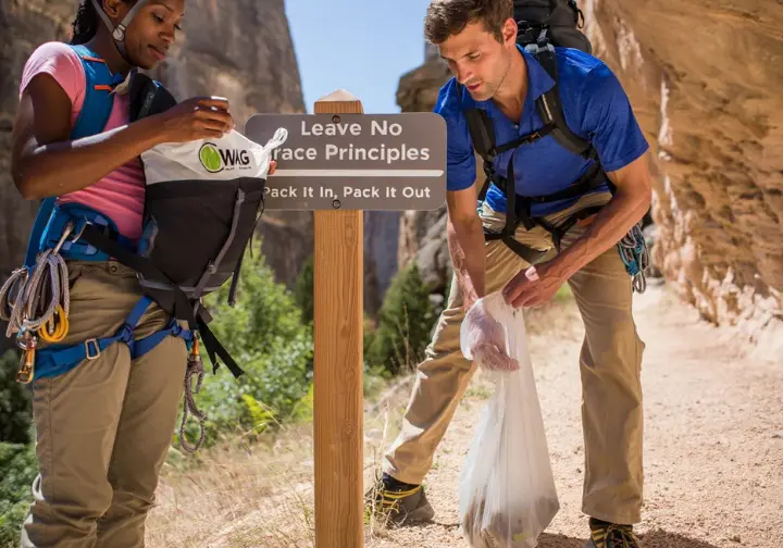 Diverse climbers practicing Leave No Trace ethics by packing out waste at a Ten Sleep Canyon rock climbing area, highlighting stewardship.