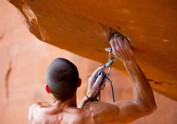 Climber using a stick clip on a Red River Gorge route, a pro tip for maximizing success and enjoyment on an RRG climbing trip.