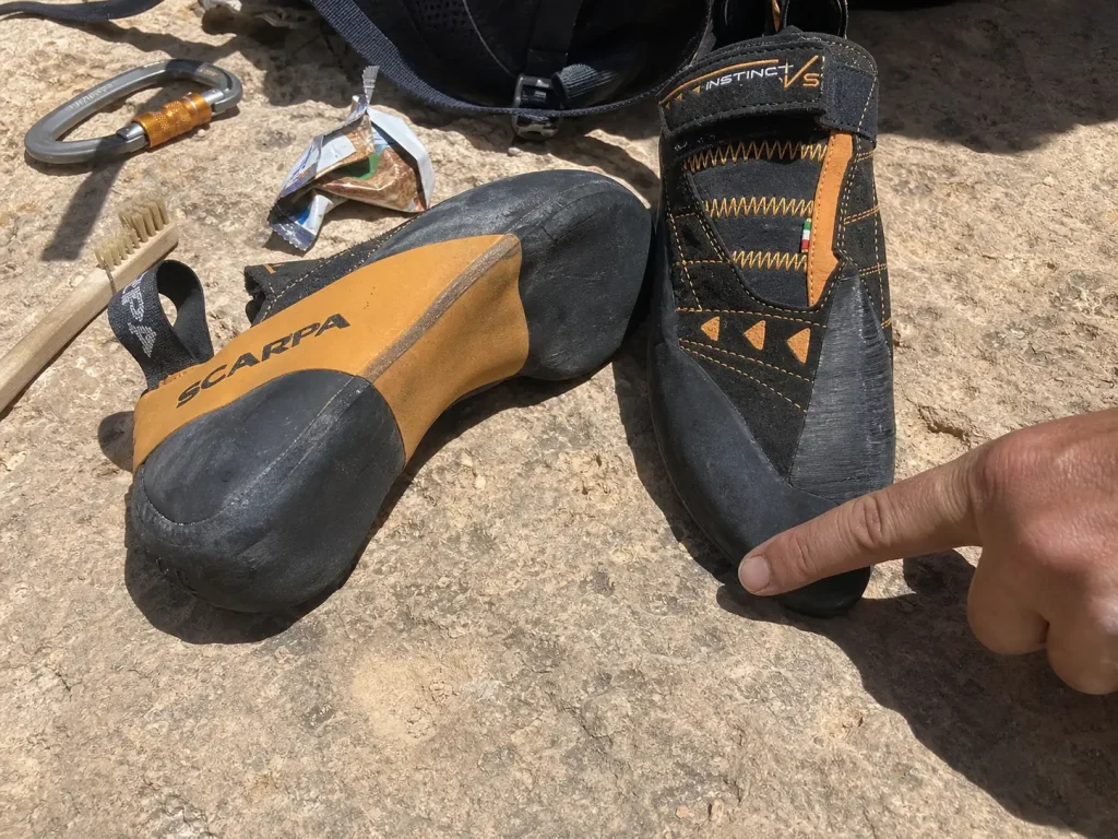 Two climbing shoes set side by side on rock showing the difference between downturn and asymmetry