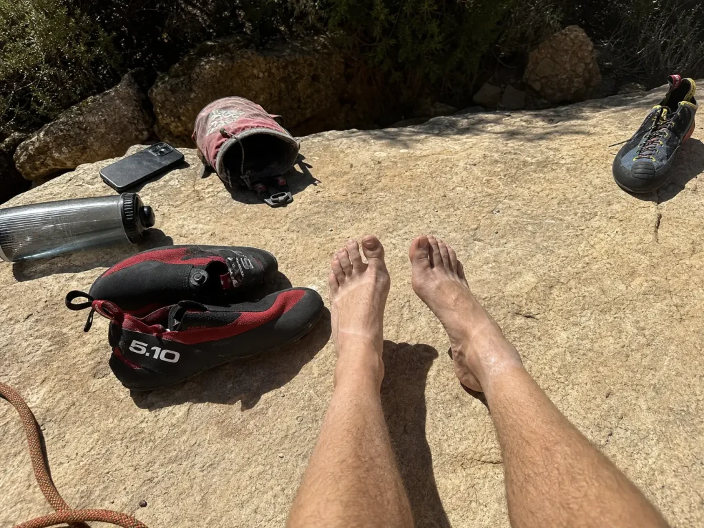 Climber resting bare feet between burns with warm-up and performance climbing shoes side by side