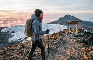 Climbing Kilimanjaro? Days Beat Fitness Every Time Trekker nearing Uhuru Peak at dawn while climbing Kilimanjaro above the clouds