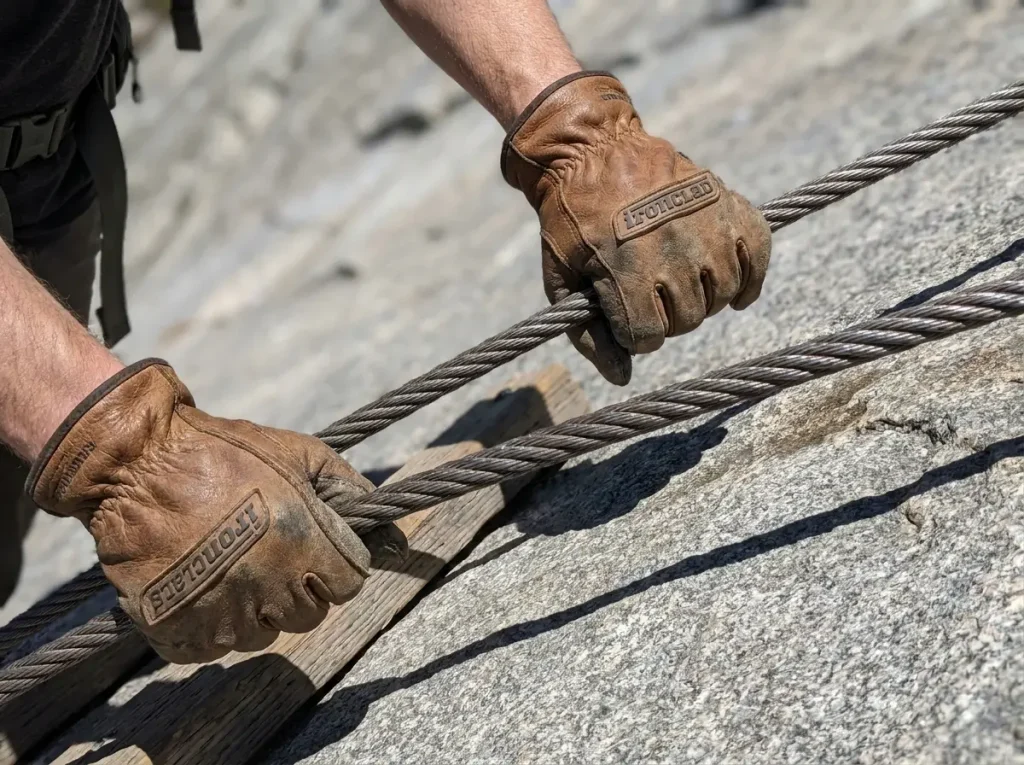 Close-up of leather-gloved hands gripping the steel cables on Half Dome's granite slab