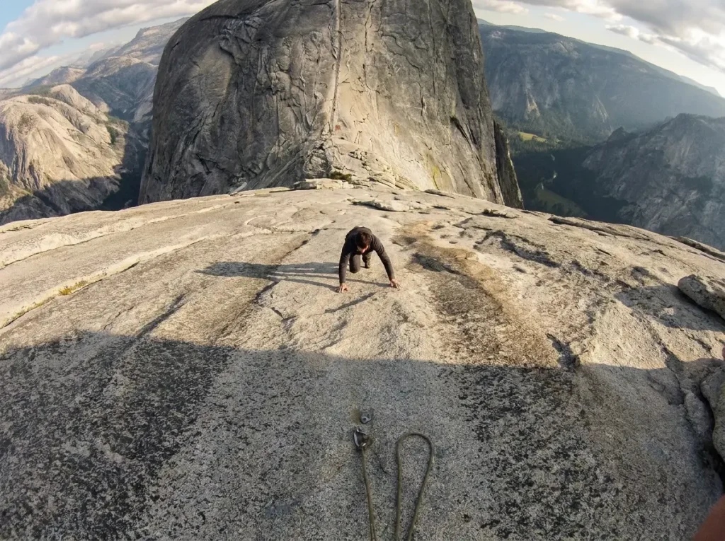Climber far above the last bolt on Half Dome's runout granite slab showing the exposure