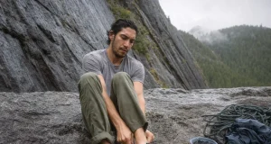 Why 98% of Climbers Buy Climbing Shoes Too Tight Climber sitting on a crag boulder easing on a Butora Endeavor climbing shoe before a route