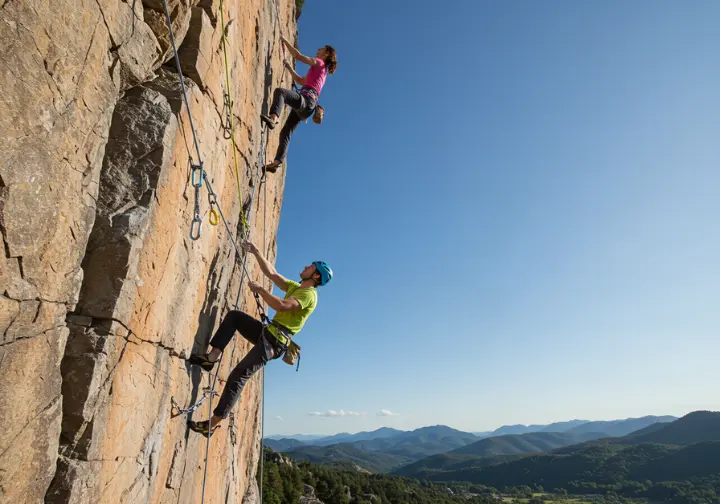 Climbers demonstrating core principles of mechanical advantage in a rock climbing pulley system on a sunny rock face.