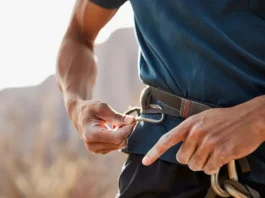 Climber's hands carefully inspecting a climbing harness to determine its true lifespan, illustrating a key aspect of how long a climbing harness lasts and when to decide on replacement.