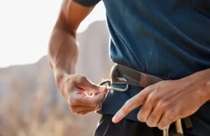 True Harness Lifespan: Inspect & Decide Now Climber's hands carefully inspecting a climbing harness to determine its true lifespan, illustrating a key aspect of how long a climbing harness lasts and when to decide on replacement.