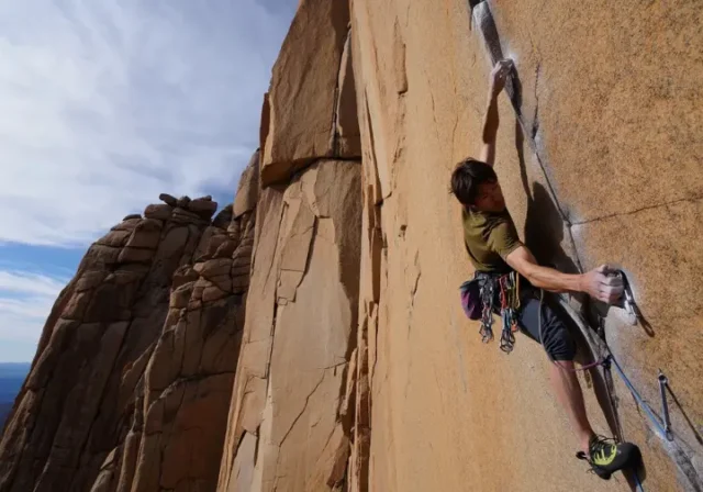 Climber placing protection on a vast cliff, illustrating the depth of understanding trad climbing beyond just the gear, a key aspect of what is trad climbing.