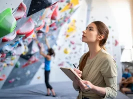 Climber thoughtfully analyzing a bouldering wall with a notebook, symbolizing a systematic approach to unlock potential and get better at bouldering.