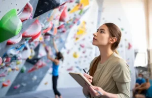 Unlock Bouldering Potential: Get Better Systematically Climber thoughtfully analyzing a bouldering wall with a notebook, symbolizing a systematic approach to unlock potential and get better at bouldering.